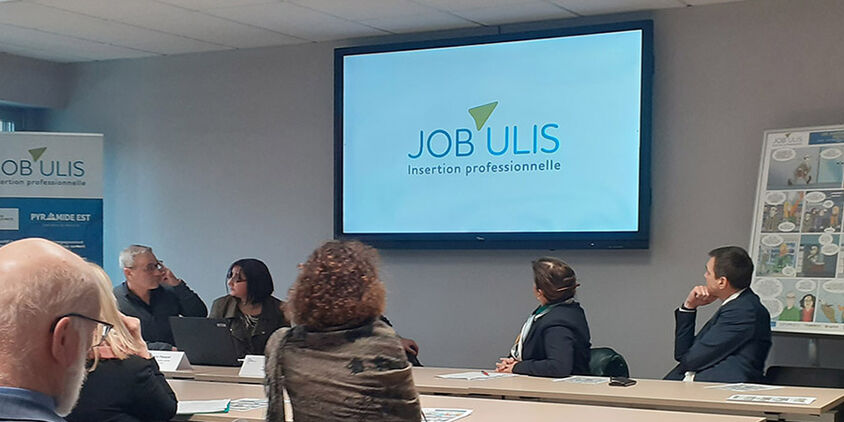 Photo de la réunion avec la projection d'une vidéo avec le logo JOB'ULIS apparaissant sur un grand écran.