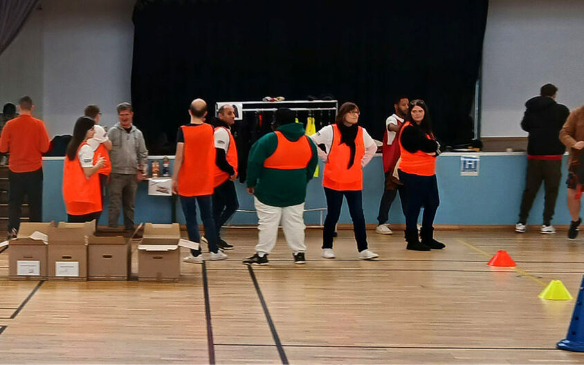 Plusieurs demandeurs d'emploi portant un dossard orange dans un gymnase pour un événement innovant afin être recruté autrement, via 10 ateliers multisports.