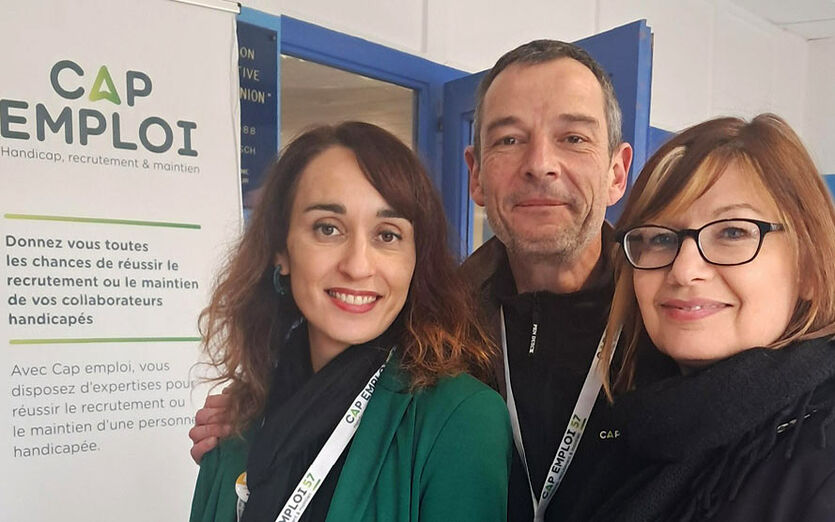 Un chargé de mission et deux chargée de mission posent devant un stand Cap emploi sur le forum.
